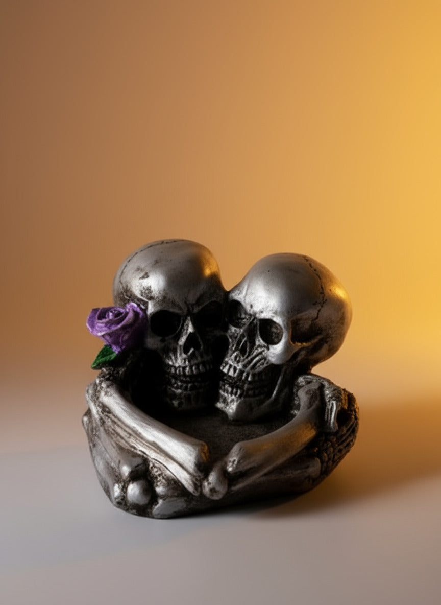 Decorative figurine of two skulls with a purple flower on a dark surface