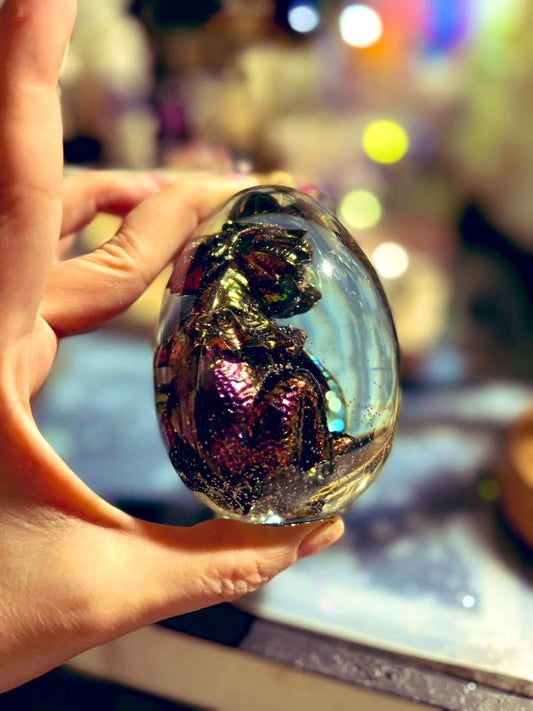 Hand holding a crystal ball with a colorful beetle inside, blurred background